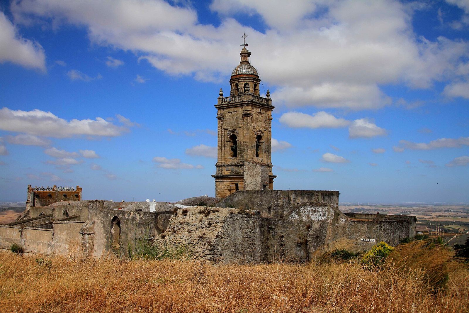 Las murallas del alcázar de Medina Sidonia y la torre de Santa María, con la hierba ya seca y dorada del verano