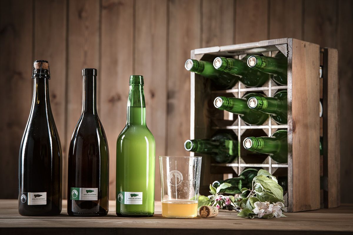 Botellas de sidra natural de Asturias con un vaso y un culín servido, sobre madera